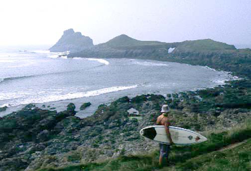 Surfer with hat looking at the break on summer days with a silhouetted headland