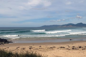 A beautiful bay with perfect beach break , distant hills on horizon